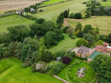 Aerial view of a property with trees fields a house and a garden with a circular path at Manor Cottage in Northallerton