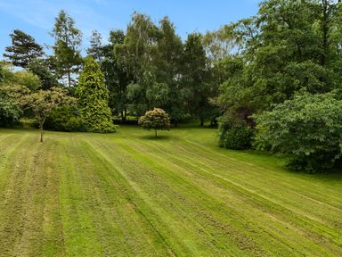 A large mowed grassy garden area with scattered trees and dense tree line in the background at Manor Cottage in Northallerton