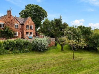 A brick house with multiple windows surrounded by green lawn and various trees at Manor Cottage in Northallerton
