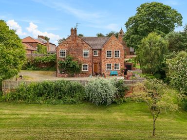 A brick house with multiple windows and a tiled roof surrounded by trees and grass at Manor Cottage in Northallerton