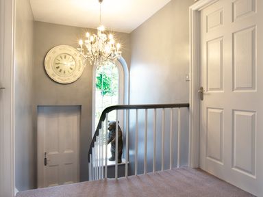 A stairway landing with a chandelier, a large wall clock, a bear statue on a window sill and a white door at Penlaurel in Launceston