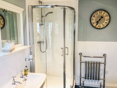 A bathroom with a glass shower enclosure a sink with faucets a wall-mounted mirror a towel radiator and a wall clock at Penlaurel in Launceston