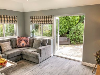 A living room with a grey sectional sofa with bear themed pillows and a door open to a patio with outdoor seating at Penlaurel in Launceston