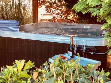 An outdoor hot tub with bubbling water beside a table holding a bottle of champagne two glasses and a plate of strawberries surrounded by greenery at Penlaurel in Launceston