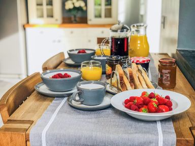 A kitchen table set with bowls of cereal with raspberries cups of milk glasses of orange juice toast in a rack jars of preserves and a plate of strawberries and raspberries at Penlaurel in Launceston