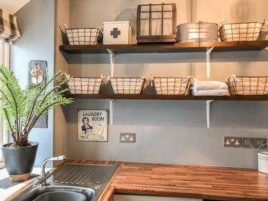 A laundry room with wire baskets on wooden shelves a metal sink a potted plant and a laundry room sign at Penlaurel in Launceston