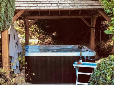 An outdoor hot tub under a wooden gazebo with robes hanging and a small table with champagne and glasses at Penlaurel in Launceston