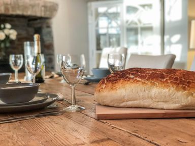A dining table set with a large loaf of bread wine glasses and a bottle at Penlaurel in Launceston