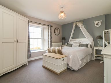 A bedroom with a bed draped with white fabric a wardrobe bedside tables and a chest at Penlaurel in Launceston
