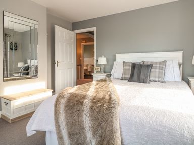 A bedroom with a bed with pillows and a blanket a mirror on the wall and a bench at Penlaurel in Launceston