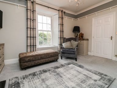 A sitting room with an armchair and ottoman near a window with checked curtains at Penlaurel in Launceston