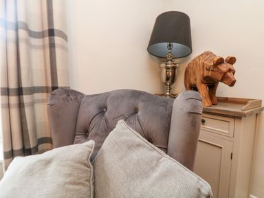 A gray upholstered armchair with beige cushions next to a cabinet with a lamp and wooden bear sculpture at Penlaurel in Launceston