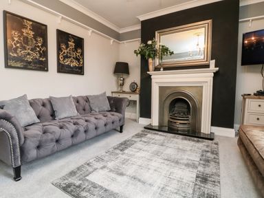 A living room with a gray tufted sofa, fireplace with a large mirror above, two framed pictures on the wall at Penlaurel in Launceston