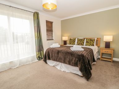 A bedroom with a bed with brown and green pillows and brown blanket with two nightstands and lamps at Ladybird in Bridgwater