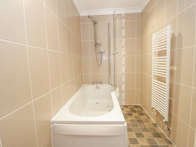A bathroom with a bathtub shower combination and a white towel radiator on tiled walls at Ladybird in Bridgwater