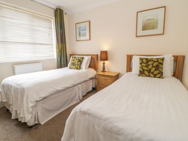 A bedroom with two single beds a bedside table with a lamp and framed pictures on the wall at Ladybird in Bridgwater
