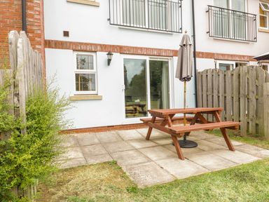 A backyard patio with a wooden picnic table and umbrella outside a house at Ladybird in Bridgwater
