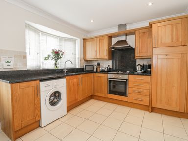 A kitchen with wooden cabinets a washing machine an oven and a vase with flowers on the windowsill at Ladybird in Bridgwater