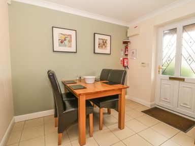 A dining area with a wooden table four black chairs a bowl placemats two framed pictures on a green wall and a white door with frosted glass at Ladybird in Bridgwater