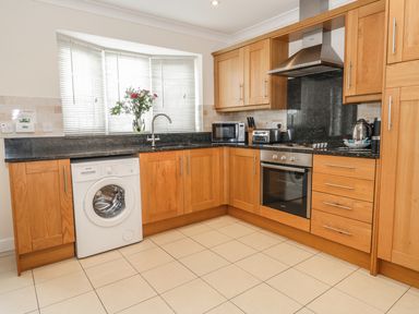 A kitchen with wooden cabinets a washing machine an oven a microwave and a vase with flowers on the windowsill at Ladybird in Bridgwater