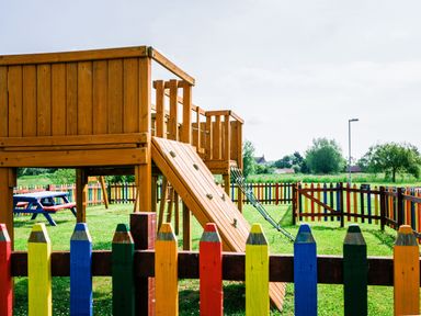 A children's playground with a wooden climbing structure and colorful picket fence at Ladybird in Bridgwater