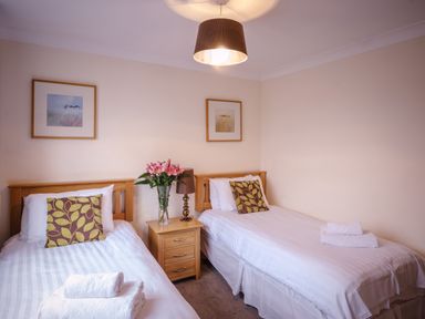 A bedroom with two single beds bedside table with flowers lamp and framed pictures on the walls at Ladybird in Bridgwater