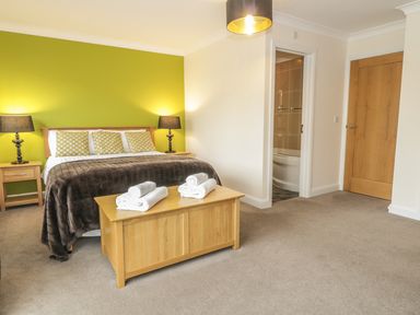 A bedroom with a bed pillows bedside tables lamps and an open door to a bathroom at Dragonfly in Bridgwater