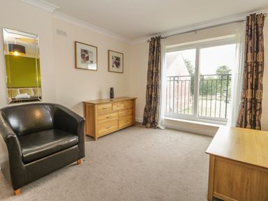 A room with a black armchair wooden dressers framed pictures on the wall and large window with curtains at Dragonfly Bridgwater