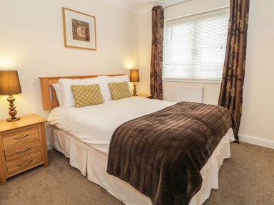 A bedroom with a bed with polka dot pillows brown blanket bedside tables with lamps window with blinds and curtains at Dragonfly in Bridgwater