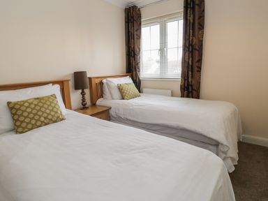 A bedroom with two single beds a bedside table with a lamp and a window with blinds and curtains at Dragonfly in Bridgwater