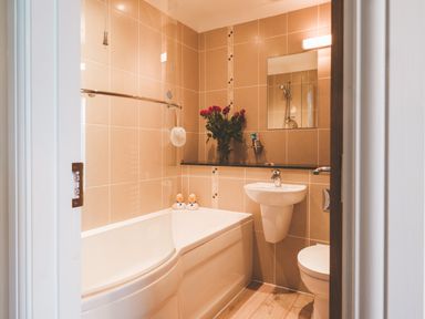 A bathroom with a bathtub, sink, toilet, mirror, and vase with red roses at Dragonfly in Bridgwater