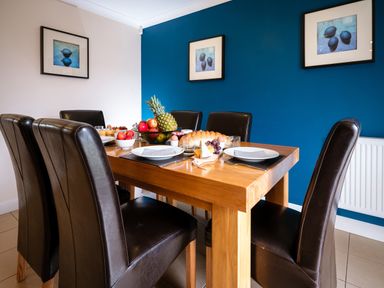 A dining room with a wooden table set with plates fruit and bread and dark brown chairs at Dragonfly in Bridgwater