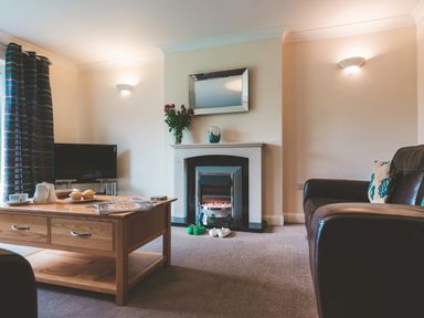 A living room with a wooden coffee table a television a fireplace with a mirror and flowers and leather sofas at Dragonfly in Bridgwater