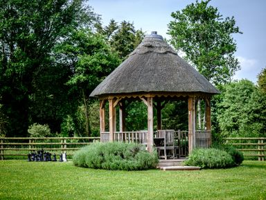 A wooden gazebo with a thatched roof in a garden with outdoor furniture and a large chess set in Bridgwater