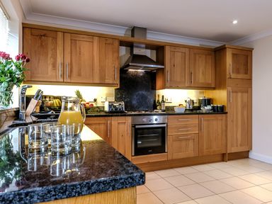 A kitchen with wooden cabinets black countertops a stainless steel oven a jug of juice and glasses on the counter at Dragonfly in Bridgwater