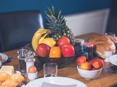 A dining table with a fruit bowl containing bananas pineapple apples lemon and orange eggs bread jars and salt and pepper at Dragonfly in Bridgwater