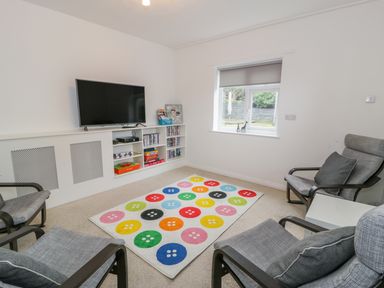 A sitting room with a wall mounted television four chairs a colourful button patterned rug and a window at Hendre Wylan in Llanaber
