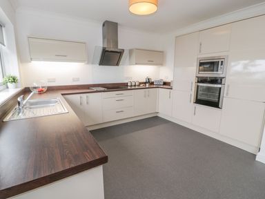 A kitchen with white cabinets brown countertops a sink stovetop built in microwave and oven at Hendre Wylan in Llanaber