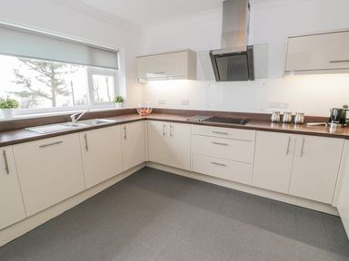 A kitchen with white cabinets a window with plants a stove and a sink at Hendre Wylan in Llanaber