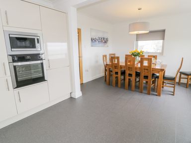 A kitchen with built in microwave and oven next to a wooden dining table with eight chairs at Hendre Wylan in Llanaber