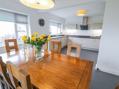 A kitchen and dining area with a wooden table and chairs and yellow flowers in a vase at Hendre Wylan in Llanaber