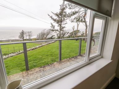 A window view showing a green lawn with trees and a railing overlooking the sea at Hendre Wylan in Llanaber