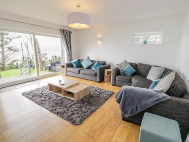 A living room with gray sofas and blue cushions beside a large glass door at Hendre Wylan in Llanaber