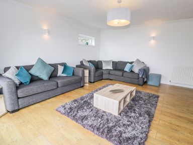 A living room with two gray sofas and blue cushions around a wooden coffee table on a gray rug at Hendre Wylan in Llanaber