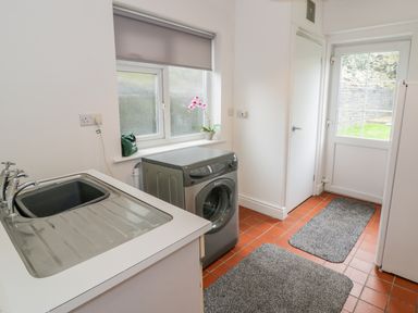 A utility room with a sink, washing machine, window with a blind, and a door leading outside at Hendre Wylan in Llanaber