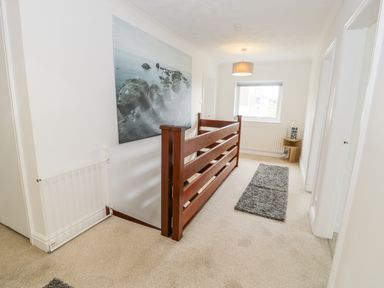 A hallway with a wooden railing a gray carpet runner and a large wall picture at Hendre Wylan in Llanaber