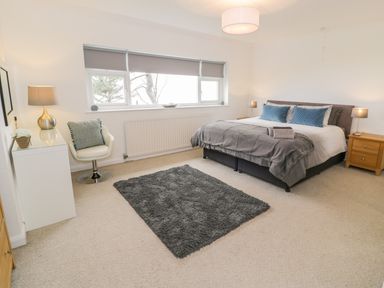 A bedroom with a bed two bedside tables a chair a dresser with a lamp and a rug on the floor at Hendre Wylan in Llanaber
