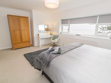 A bedroom with a bed gray blankets towels wooden wardrobe white desk chair and window blinds at Hendre Wylan in Llanaber