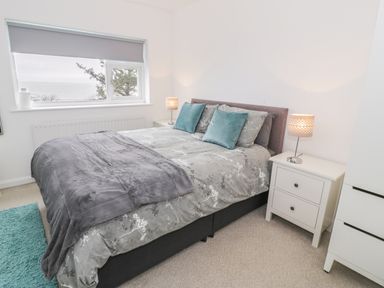 A bedroom with a bed pillows bedside tables lamps window and a carpet at Hendre Wylan in Llanaber