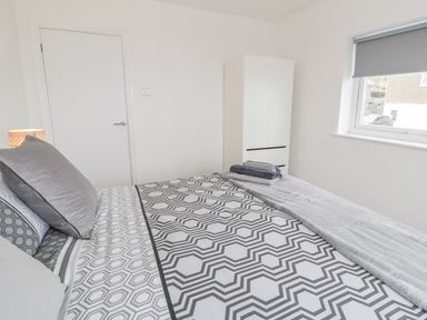 A bedroom with a bed covered in geometric patterned bedding a white wardrobe and a window with a gray blind at Hendre Wylan in Llanaber